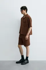 Bermuda de corte relajado color marrón con finas rayas verticales negras. Presenta cintura elástica ajustable con cordón y bolsillos laterales y trasero.