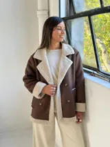 Tapado de estilo aviador en color chocolate con interior y detalles de corderito en color beige. Presenta cierre frontal cruzado con botones, solapas amplias y puños con borde de corderito.