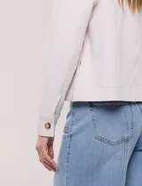 Camperita corta blanca de punto elastizado, con cuello camisero, cierre frontal completo y mangas largas con puños anchos abotonados.