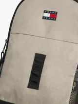 Mochila outdoor Tommy Jeans color beige con base negra, bolsillo principal con cierre, bolsillos laterales de red y asa superior. Cuenta con detalles distintivos de la marca y logo bordado en el frente.