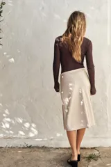 Falda corta tipo pareo, color marrón oscuro, confeccionada en tejido satinado con lazada ajustable en el lateral.