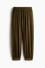 Pantalón globo verde militar de corte holgado en tejido con leve brillo, con elástico fruncido y cordón ajustable en la cintura, bolsillos laterales y puños abotonados en el bajo.