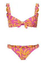 Conjunto de bikini marca Triya con estampado de bananas rosas y amarillas. El corpiño es de tirantes con volados y tiene un lazo extraíble. La bombacha tiene volados laterales.