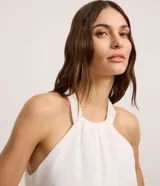 Mono largo blanco de crepé, con cuello halter, sin mangas y superposición fruncida en el tronco. Se ata con lazo en la nuca.