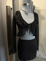 Top de tul negro con mangas largas, escote profundo con volados y cierre frontal con lazo para anudar.