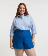 Camisa plus size alargada confeccionada en tela anarruga a rayas verticales celestes y blancas, con cuello inglés, botones delanteros para cierre y mangas largas con puños abotonados.