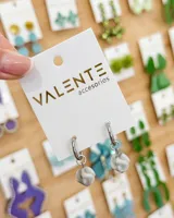 Aros tipo argolla de acero con dije colgante esférico de piedra veteada en tonos gris y blanco.