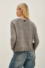 Cardigan de tejido de punto color beige melange, con escote en V y cierre frontal de botones plateados. Presenta mangas largas con puños acanalados.