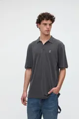 Remera polo de manga corta de algodón piqué lavado, color gris oscuro, con cuello y puños acanalados con detalles de líneas. Cuenta con media cartera de botones, calce clásico y bordado pequeño en el pecho.