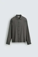 Camisa de corte relajado confeccionada en tejido fluido con mezcla de modal, presenta un diseño de rayas verticales con textura efecto arrugado, cuello solapa, cierre frontal de botones y manga larga con puños abotonados.