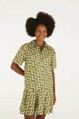Vestido corto de algodón con estampado geométrico de ondas en tonos verde, amarillo y blanco, con cuello camisero, manga corta y cierre frontal de botones.
