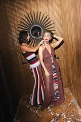 Vestido largo de encaje y transparencias color marrón, con escote profundo halter, frunces en el cuerpo, espalda abierta y tiras largas estampadas para atar al cuello.