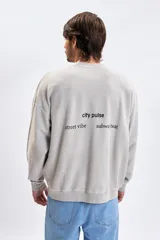 Sudadera de cuello redondo con efecto lavado, confeccionada en tejido de textura suave. Presenta un corte holgado con hombros caídos y puños y ruedo acanalados. Incluye una pequeña estampa minimalista en el pecho.