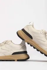 Zapatillas deportivas color crema con detalles en beige, negro y blanco.
