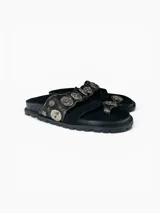 Sandalias planas de cuero negro con diseño de tiras anchas decoradas con apliques metálicos circulares grabados. Presentan una tira separadora para el dedo y plantilla forrada en cuero.