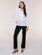 Camisa blanca de corte clásico y caída fluida, con cuello camisero tradicional, abotonadura frontal oculta y mangas largas con puños anchos.