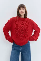 Sweater de punto grueso color rojo, con cuello alto y diseño de relieves tipo pompones en el frente y las mangas. Presenta puños y ruedo acanalados.