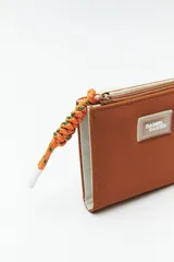 Billetera compacta de símil cuero color celeste claro, con cierre superior y un tirador de cordón trenzado multicolor. Posee un parche frontal con el logo de la marca.