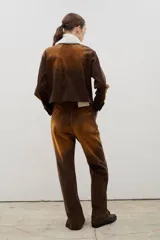 Pantalón de tiro alto confeccionado en pana, con corte recto y efecto gastado en degradé que transiciona de tonos oscuros a ocre. Presenta un cierre frontal con botones visibles y costuras a contratono.