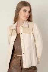 Camisa de cuero ovino color beige claro, estilo western, con canesú en los hombros en gamuza de tono similar. Presenta costuras contrastantes y cierre frontal con broches. Posee bolsillos laterales.