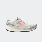 Championes de running New Balance modelo 1080 v15, color blanco con detalles en gris y logo lateral con degradado en rosa y naranja. Presentan una parte superior de malla transpirable y una mediasuela con tecnología Infinion para mayor amortiguación y retorno de energía.
