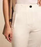 Pantalón de sastrería estilo carrot color blanco, de tiro alto, con trabillas en la cintura y cierre frontal de cremallera y botón.