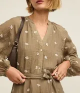 Vestido largo evasê color marrón con estampado de flores blancas, cuello en V, mangas largas abullonadas y cinturón de lazo.