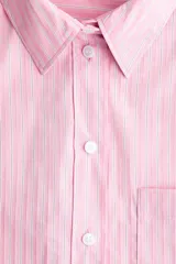 Camisa oversized a rayas color rosado y blanco, con cuello clásico, cierre frontal de botones, un bolsillo aplicado en el pecho y mangas largas con puños abotonados.