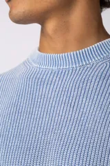 Sweater de punto grueso con textura waffle, de calce relajado y cuello redondo. Presenta puños y ruedo acanalados, con un pequeño parche con logo en el puño izquierdo.