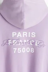 Buzo canguro lila con capucha, corte holgado, hombros caídos, bolsillo delantero y puños y bajo acanalados. Estampado con la frase "Paris, France" y "Le Triangle d'Or".