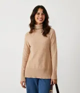 Suéter de tejido de punto color beige con cuello alto, mangas con corte raglán y puños y ruedo acanalados. Presenta un diseño clásico y cómodo con el ruedo trasero ligeramente más largo.