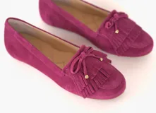 Mocasines de cuero gamuzado color fucsia, con flecos y un lazo con herrajes metálicos dorados en la capellada. Suela plana de goma.