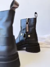 Bota corta negra de cuero, con caña media, hebilla lateral y suela track.