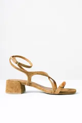 Sandalias de taco cuadrado medio, confeccionadas en gamuza color tostado. Presentan tiras finas cruzadas, pulsera al tobillo con hebilla metálica y detalle de cuentas decorativas en la tira frontal.