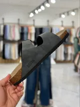 Sandalias de dos tiras negras con hebillas metálicas ajustables, plantilla anatómica y suela plana.