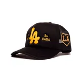 Gorro trucker negro con diseño de red en la parte trasera, visera curva y bordado frontal en hilo amarillo con las letras 'LA' y las leyendas 'Mi CASA' y 'Su CASA'.