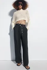 Pantalón de lino negro de tiro medio, con pernera recta, pinzas delanteras y detalle de puntilla en la cintura. Cuenta con bolsillos frontales y cierre con cremallera y botón.