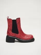 Bota tipo chelsea de cuero vacuno en color rojo con estampado floral grabado en negro. Presenta paneles laterales elásticos, suela de plataforma y taco cuadrado en color negro.