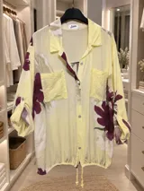 Camisa blanca de manga larga con estampado floral en tonos bordó y verde, cuello camisero, cierre frontal de botones y bolsillos en el pecho con apliques de lentejuelas.