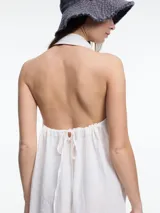 Vestido largo de lino en color azul, con cuello camisero, cierre frontal de botones y espalda descubierta con diseño estilo halter. Presenta un bordado decorativo en el cuello y bolsillos laterales.