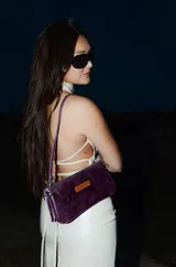 Mini cartera de cuero color violeta metalizado, con diseño rectangular, cierre superior y correa corta para llevar al hombro.