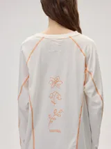 Remera manga larga de algodón color crudo, con cuello redondo y calce holgado. Posee costuras a la vista en color naranja y un delicado bordado con la frase "the flower edit" sobre el hombro izquierdo.