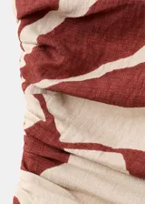 Vestido midi entallado de diseño asimétrico con un solo hombro y una manga larga, confeccionado en color beige con estampado de hojas en tonos bordó. Presenta un cuerpo fruncido y detalle drapeado.