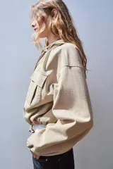 Cazadora color beige con capucha ajustable, manga larga con puño elástico, bolsillos frontales con solapa, bajo ajustable y cierre frontal con cremallera y botones a presión.