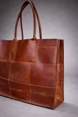 Bolso tote grande de cuero natural en color marrón, con diseño de piezas unidas mediante costuras visibles y asas de hombro.