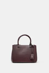Bolso pequeño tipo satchel, color borgoña oscuro, con doble asa de mano y correa bandolera extraíble. Presenta dos compartimentos exteriores con cierre de cremallera metálica y un compartimento interior con cierre imantado.