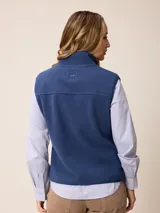 Chaleco de sherpa color beige con cierre frontal completo, cuello alto y bolsillo con cierre en el pecho que incluye un detalle circular con logo.