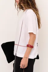 Blusa de lino color beige, de corte recto y mangas cortas, con costuras decorativas pespunteadas en tono rojizo que forman líneas verticales y horizontales.