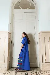Vestido largo verde militar de popelina de algodón, con diseño oversized, cuello mao, mangas cortas, bolsillos laterales y cierre frontal con botones. Presenta un estampado de flores grandes en la parte superior y franjas horizontales de colores en el ruedo.