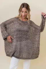 Buzo de tejido liviano y calado con brillo sutil, color gris oscuro o negro. Presenta un calce amplio y mangas amplias, con un detalle de tiras entrelazadas en la espalda. El largo es irregular, más largo en la parte trasera.